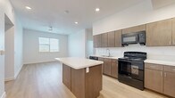 This 2-bedroom, 2-bathroom unit in Austin, TX offers a well-designed, single-floor layout with a clean, contemporary aesthetic. The open-concept kitchen serves as the heart of the home, showcasing warm medium-toned wood cabinetry, a white quartz-topped center island with built-in storage, a full suite of black appliances including a gas range, dishwasher, and refrigerator, and a subway tile backsplash. Light wood-look flooring flows seamlessly through the kitchen and into the living area, which benefits from natural light through a sizable window and a ceiling fan overhead. Both bedrooms are bright and airy, featuring the same wood-look flooring, crisp white walls, and windows that invite natural light. The primary bedroom offers a comfortable footprint well-suited for a full furniture arrangement. The two bathrooms are finished with large-format tile flooring, warm wood vanities with integrated sinks, and clean white walls. One bathroom features a walk-in shower with grab bars, adding practical accessibility. Hallways connect the spaces efficiently, giving the overall layout a logical, easy-to-navigate flow. The unit's consistent use of neutral tones and modern finishes creates a cohesive and functional living environment.