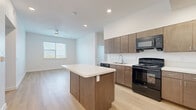 This 2-bedroom, 2-bathroom unit in Austin, TX offers a well-designed, single-floor layout with a clean, contemporary aesthetic. The open-concept kitchen serves as the heart of the home, showcasing warm medium-toned wood cabinetry, a white quartz-topped center island with built-in storage, a full suite of black appliances including a gas range, dishwasher, and refrigerator, and a subway tile backsplash. Light wood-look flooring flows seamlessly through the kitchen and into the living area, which benefits from natural light through a sizable window and a ceiling fan overhead. Both bedrooms are bright and airy, featuring the same wood-look flooring, crisp white walls, and windows that invite natural light. The primary bedroom offers a comfortable footprint well-suited for a full furniture arrangement. The two bathrooms are finished with large-format tile flooring, warm wood vanities with integrated sinks, and clean white walls. One bathroom features a walk-in shower with grab bars, adding practical accessibility. Hallways connect the spaces efficiently, giving the overall layout a logical, easy-to-navigate flow. The unit's consistent use of neutral tones and modern finishes creates a cohesive and functional living environment.