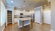 This two-story residence offers 3 bedrooms and 4 bathrooms across a thoughtfully designed floor plan. The ground floor serves as the main living and functional hub, featuring a contemporary kitchen equipped with white shaker-style cabinetry, taupe quartz countertops, stainless steel appliances including a refrigerator, range, and microwave, and a central island with pendant lighting overhead. Wood-look flooring runs throughout the main level, adding warmth to the neutral gray and white color palette. A hallway connects the primary areas, and a staircase with clean white railings leads to the upper floor. One bathroom on the main level features a compact water closet layout with matching wood-look tile flooring.

The upper floor is slightly larger than the ground floor and houses all three bedrooms, each carpeted and featuring windows that allow natural light. The bedrooms are finished with neutral gray walls and white baseboards, maintaining a consistent, modern aesthetic. The bathrooms upstairs include a full bath with a white vanity, tile flooring, and a tub-shower combination. A dedicated laundry room on the upper level accommodates a full-size washer and dryer. Two closets provide additional storage throughout the home.