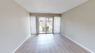 Located at 2909 Gulf to Bay Blvd in Clearwater, Florida, this single-floor unit offers a clean, well-maintained interior with a light and airy aesthetic throughout. The living area is a standout feature, showcasing light hardwood-style flooring that extends seamlessly across the space. Large sliding glass doors flanked by vertical blinds fill the room with natural light and provide direct views of the outdoor greenery, creating a bright and welcoming atmosphere. An adjacent dining or flex area continues the hardwood-style flooring and includes a pendant light fixture, with a paneled entry door completing the entryway. The kitchen is efficiently designed with white cabinetry, light quartz-style countertops, a stainless steel double sink, and a full suite of appliances including an electric range. A window above the sink allows for additional natural light. The bedroom is generously proportioned, featuring plush carpeting for comfort and a sliding closet with built-in rod and shelving for ample storage. The bathroom area includes white cabinetry with a light countertop, a large mirror, and built-in shelving nearby, with easy access to the bedroom. The unit's neutral color palette and updated finishes contribute to a cohesive, move-in-ready feel throughout.