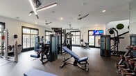 Located at 300 Dalhausser Lane in Oviedo, FL, this two-story fitness center is a comprehensively equipped facility designed to support a wide range of workout needs. The lower level provides a solid foundation for the facility, while the more expansive upper floor offers additional training space, together creating a well-organized and functional environment.

The gym areas are outfitted with professional-grade Matrix equipment, including multi-station cable machines, weight benches, a full rack of dumbbells, and an assortment of cardio machines such as treadmills, ellipticals, and stair climbers. Large black-framed windows throughout the gym spaces flood the floors with natural light and provide outdoor views, contributing to an energizing atmosphere. Ceiling fans and modern lighting fixtures — including linear LED pendants — maintain comfort and visibility across the workout areas.

Design details such as exposed wood beams, a bold teal ceiling accent, and a vibrant graphic accent wall add visual character to the space. Full-length mirrors in the free weights area enhance both functionality and the sense of openness. Rubber flooring throughout ensures durability and safety.

The facility also includes a cedar-lined sauna, offering a dedicated recovery space. Supporting amenities include multiple utility rooms, two bathrooms, a connecting hallway, and two staircases providing convenient access between floors.