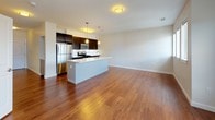 Located at 6 Upland Woods Circle in Westwood, MA, this single-floor, one-bedroom, one-bathroom residence offers a thoughtfully designed layout with contemporary finishes throughout. The open-concept living and kitchen area is anchored by rich hardwood flooring that extends across the main living space, creating a warm and cohesive atmosphere. The kitchen is outfitted with dark espresso-toned cabinetry, stainless steel appliances including a gas range, built-in microwave, and refrigerator, along with a white quartz countertop and a central island with an integrated sink. Pendant lighting above the island complements the overall modern aesthetic. The living area is generously proportioned, with multiple windows allowing natural light to fill the space. The bedroom features soft carpeting, a large window with exterior views, and access to a spacious walk-in closet equipped with wire shelving on multiple walls, offering ample storage. The full bathroom includes dark wood vanity cabinetry, a white quartz countertop, a framed mirror, and a full tub-shower combination with tile surround, all set on neutral large-format tile flooring. The unit's clean, neutral palette and modern design elements create a comfortable and functional living environment.