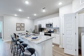 This single-story residence in Pensacola, Florida, offers a thoughtfully designed layout with modern finishes throughout. The kitchen serves as a central highlight, featuring crisp white shaker cabinetry, light granite countertops, a classic subway tile backsplash, and a full suite of stainless steel appliances. A spacious island with bar seating provides both additional prep space and a casual dining option, complemented by recessed lighting overhead and light wood-look flooring that extends throughout the home.

The living area is bright and welcoming, with a ceiling fan, recessed lighting, and a set of glass-paned doors that invite natural light and provide outdoor access. The neutral color palette creates a calm, cohesive atmosphere across all rooms.

The bedroom is generously sized, featuring a ceiling fan and soft neutral walls that contribute to a restful environment. The bathroom offers white cabinetry with granite countertops, a large mirror, and convenient built-in open shelving for storage. An adjacent walk-in closet adds practical functionality to the space.

A second bathroom, accessible from the main living area, mirrors the same refined finishes, maintaining consistency throughout the home. Overall, the residence presents a clean, contemporary aesthetic well-suited to comfortable everyday living.