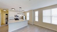 Located at 1910 Capital Creek Dr in Wake Forest, NC, this two-story home offers a thoughtfully designed open-concept floor plan that seamlessly connects the kitchen and living areas. The kitchen is a standout feature, showcasing white cabinetry, a subway tile backsplash, light quartz countertops, and a peninsula island ideal for casual dining or meal prep. Stainless steel appliances, including a refrigerator, range, and over-the-range microwave, complete the modern culinary space. Stylish pendant lighting with an industrial-inspired design hangs above the island, adding character and warmth. The adjoining living area is bathed in natural light from multiple large windows dressed with clean white blinds, creating a bright and welcoming atmosphere. Durable wood-look flooring flows throughout the main living areas, providing both aesthetic appeal and practicality. Neutral warm-toned walls complement the light finishes throughout, contributing to an airy and cohesive design. Spanning two floors, the home provides ample space for comfortable everyday living, with the upper level offering additional privacy and separation from the main living areas.