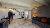 Located at 1503 Monmouth Ave in Lancaster, Ohio, this two-floor home offers a practical and well-organized layout with distinct living spaces across both levels. The main floor features an open-concept design where the living area and kitchen flow seamlessly together, connected by light wood-look flooring throughout. The kitchen is equipped with grey cabinetry, granite-style countertops, a mosaic tile backsplash, black appliances including a full-size refrigerator, and ample counter space for meal preparation. Exposed ceiling beams add a subtle architectural character to the main living area, which is bathed in natural light from a front-facing window near the entry door. A full bathroom on the main level features grey walls, a granite-top vanity, and wood-look flooring. A dedicated laundry area accommodates a full-size washer and dryer alongside a water heater. A striking white metal open-riser staircase serves as a central visual feature, connecting the two floors. The upper level hosts a carpeted bedroom with grey walls, a ceiling fan with light fixture, a natural light window, and a closet. The overall color palette of cool greys, white trim, and warm wood tones gives the home a cohesive and contemporary feel throughout.