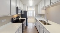 This single-floor residence offers a thoughtfully designed layout with a neutral color palette and a clean, move-in-ready aesthetic throughout. The galley-style kitchen is a functional highlight, featuring white shaker cabinetry, quartz countertops, stainless steel appliances including a range, microwave, refrigerator, and dishwasher, along with wood-look flooring and ample overhead lighting. The kitchen opens toward a spacious living area finished with plush wall-to-wall carpeting and neutral gray walls, providing a versatile canvas for any furnishing style. Sliding glass doors in the living space invite natural light and offer access to an outdoor area, extending the sense of openness. The bedrooms are generously sized with soft carpeting, large windows fitted with horizontal blinds, and dedicated closet space — one bedroom features a walk-in closet, offering excellent storage. The bathroom is well-equipped with white cabinetry including an overhead cabinet with an open shelf, a vanity with ample counter space, chrome fixtures, and wood-look tile flooring. The 3D dollhouse view confirms a compact yet efficient floor plan that maximizes usable space across all rooms, making this a practical and comfortable living space.