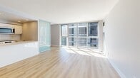 Located on the 18th floor at 235 Bloor Street East in Toronto's vibrant Bloor-Yorkville neighbourhood, this two-bedroom, one-bathroom unit offers a well-designed layout with modern finishes throughout. Light hardwood flooring runs through the living areas and bedrooms, complementing the unit's bright, neutral palette.

The open-concept living room is bathed in natural light through expansive floor-to-ceiling windows and sliding glass panels that frame sweeping views of the Toronto skyline. A frosted glass sliding partition adds a contemporary architectural touch to the space.

The kitchen is thoughtfully appointed with white flat-panel cabinetry, white quartz countertops, a subway tile backsplash, and a full suite of stainless steel appliances including a refrigerator, dishwasher, electric range, and built-in microwave. Recessed lighting and light tile flooring complete the clean, functional design.

The primary bedroom offers generous proportions with large windows overlooking the city, while the second bedroom provides a comfortable, versatile space. The full bathroom features a soaker tub with overhead shower, white tile surround, and chrome fixtures. A dedicated laundry area adds everyday convenience to this well-appointed urban residence.