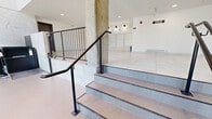 Located at 5480 Avenue Henri-Julien in the Plateau-Mont-Royal area of Montréal, this building lobby offers a clean, contemporary first impression. The space is finished with large-format porcelain tiles in a marble-effect white throughout, complemented by matching marble-effect wall cladding that lends a cohesive, polished aesthetic. Recessed ceiling lighting provides even illumination across the generously sized, open hallway floor plan.

A defining architectural feature is the floor-to-ceiling glazed facade near the entrance, which floods the lobby with natural light and frames views of the surrounding streetscape. The main entry is accessed via double glass doors with aluminum framing, flanked by high marble-effect walls that emphasize the verticality of the entryway. Black steel railings line the interior staircase, adding a modern industrial contrast to the light-toned finishes.

The lobby is equipped with a built-in mailbox bank for residents, a wheelchair accessibility lift, and an intercom system near the entrance. Exposed concrete structural columns punctuate the space, adding an element of raw texture against the otherwise refined surfaces. The overall ambiance is bright, accessible, and functionally well-appointed, reflecting a modern residential building designed with both aesthetics and practicality in mind.