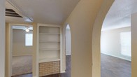 This single-floor residence offers a thoughtfully designed layout with a series of elegant arched doorways that connect the living areas, creating a sense of continuity and architectural character throughout the space. The living area is anchored by rich, dark hardwood-style flooring that extends seamlessly across the main rooms, complemented by textured ceilings that add depth to the interior. A standout feature is the built-in shelving unit with a decorative brick base, providing both functional storage and a charming design element. An exposed brick accent wall in the main living area further enhances the warm, inviting atmosphere.

The kitchen features white cabinetry, dark countertops, a double-basin sink, a dishwasher, and a pass-through window that connects to the living space, promoting an open feel. The kitchen is also equipped with a refrigerator and convenient in-unit laundry with a stacked washer and dryer unit tucked efficiently into a dedicated area.

The bathroom includes a wide vanity with dark countertops, a large wall mirror, and a full-size bathtub with a shower. Natural light filters through window blinds in multiple rooms, contributing to a bright and comfortable living environment throughout this well-appointed space.