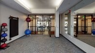 Located at 205–207 Carolina Point Pkwy in Greenville, SC, this fitness center offers a thoughtfully designed, single-floor layout that accommodates a wide range of workout modalities. The space is organized into distinct functional zones, each outfitted with professional-grade Life Fitness equipment.

The cycling area features multiple stationary spin bikes arranged to allow comfortable spacing between users. A wall-mounted mini-split air conditioning unit ensures climate control, while a large frosted window provides natural light without direct glare. TRX suspension training straps are anchored to a dedicated wall-mounted rig, supporting bodyweight and functional strength training.

An adjoining area houses stability balls of varying sizes displayed on a tiered rack, resistance bands, and a wall-mounted exercise mat, creating a versatile stretching and core training zone. A rack of weighted medicine balls adds further options for functional fitness routines.

The space is framed by floor-to-ceiling black steel and glass partitions, offering visual openness while defining separate training areas. Full-length mirrors expand the sense of space and assist with form correction. Recessed tray ceiling lighting and neutral gray carpet throughout contribute to a clean, modern aesthetic suited to a professional fitness environment.