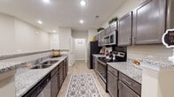 This single-story residence offers a thoughtfully designed open-concept layout that seamlessly connects the main living areas. The kitchen is a standout feature, showcasing dark espresso cabinetry, granite countertops, stainless steel appliances including a range, microwave, and refrigerator, and a double-basin sink. A galley-style configuration maximizes counter and storage space, while light wood-look flooring runs throughout the main areas, contributing to a cohesive and clean aesthetic.

A raised breakfast bar divides the kitchen from the adjoining living and dining spaces, providing both a visual anchor and functional separation. The living room is generously proportioned, featuring a ceiling fan with integrated lighting and access to a private exterior door. A dedicated dining nook accommodates a glass-top table and provides a quiet corner for meals.

The bedroom is carpeted for comfort, with a ceiling fan and ample room for furnishings. An adjacent bathroom includes a shower with a decorative curtain and standard fixtures. Recessed lighting throughout the main areas, neutral warm-toned walls, and consistent finishes give the entire space a polished, move-in-ready appearance.