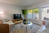 This thoughtfully designed two-story home offers a clean, modern aesthetic across its well-organized layout. The ground floor welcomes residents through a hallway that opens into a bright and airy living room, where large windows frame outdoor views and warm hardwood flooring runs underfoot. The adjacent dining area benefits from natural light streaming through a sizeable window, creating a cheerful space for everyday meals. The kitchen is equipped with white shaker-style cabinetry, a sleek quartz countertop, an undermount stainless steel sink with a contemporary coil-spring faucet, and integrated appliances. A dedicated laundry room on this level houses a full-size washer and dryer with a window above for ventilation. The upper floor accommodates three bedrooms, including a well-proportioned primary suite. The additional bedrooms feature carpet flooring, large windows with outdoor views, and built-in closets for storage. Three bathrooms serve the home, with at least one featuring large-format tile flooring, a white vanity with quartz countertop, and a glass-enclosed walk-in shower. Throughout, the home maintains a cohesive palette of soft whites and light greys, contributing to a calm and contemporary ambiance across both levels.