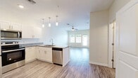 This 690 square foot apartment offers a thoughtfully designed living space that maximizes functionality and comfort. The single-floor layout features one bedroom, measuring 170 square feet, providing ample space for rest and relaxation. The open-concept living area is highlighted by large windows that flood the space with natural light, creating an airy and inviting atmosphere. 

The modern kitchen is a standout feature, boasting sleek white cabinetry, granite countertops, and stainless steel appliances. Pendant lighting adds a touch of elegance, while the breakfast bar offers additional seating and workspace. The bathroom, though not pictured, complements the apartment's one-bedroom configuration.

Throughout the apartment, you'll find a mix of flooring materials. The main living area and kitchen showcase durable, wood-look vinyl planks, while the bedroom features plush carpeting for added comfort. A ceiling fan in the bedroom provides air circulation and comfort.

Storage solutions are abundant, with a walk-in closet in the bedroom and additional closet space near the bathroom. The apartment also includes a dedicated laundry area with shelving for organization.

The neutral color palette of whites and light grays creates a blank canvas for personalization, allowing residents to easily incorporate their own style. This efficient and well-appointed apartment is ideal for singles or couples seeking a contemporary living space with all the essential amenities.
