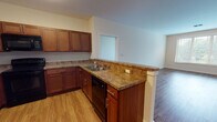 Located at 1 Overlook Dr in Monroe Township, NJ, this single-floor residence offers a well-designed layout with an open-concept living and kitchen area, multiple bedrooms, and two full bathrooms. Rich hardwood-style flooring runs throughout the main living spaces and bedrooms, contributing to a warm and cohesive aesthetic.

The kitchen is a functional centerpiece, outfitted with rich cherry wood cabinetry, granite-style countertops, and a full suite of black appliances including a refrigerator, range, microwave, and dishwasher. A peninsula with seating overhang connects the kitchen seamlessly to the open living area, which is bright and airy with natural light filtering in through large windows with blinds.

The bedrooms are generously sized, each featuring hardwood-style flooring, neutral walls, and windows that allow natural light and outdoor views of the surrounding greenery. Closet space is also present in the bedroom areas.

Both bathrooms are finished with light tile flooring and include rich wood vanities with white countertops, framed mirrors, and overhead lighting. One bathroom features a walk-in shower, while the other includes a full soaking tub with shower combination. The unit also includes an in-unit laundry area, adding everyday convenience to this well-appointed residence.