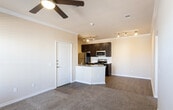 Located at 5801 Deauville Blvd in Midland, Texas, this single-floor residence offers a well-appointed, cohesive interior design throughout. The open-concept kitchen serves as a functional centerpiece, showcasing dark espresso cabinetry that reaches toward the ceiling, granite countertops, and a full suite of stainless steel appliances including a range, over-the-range microwave, and refrigerator. A white subway tile backsplash adds a clean, classic contrast to the rich cabinetry. The kitchen peninsula with an integrated sink and granite surface extends into the main living area, creating a natural transition between spaces. Crown molding and track lighting run throughout, lending a polished, finished character to the interior. Wood-style plank flooring flows through the kitchen and living areas, while plush carpet adds warmth to the bedroom, which is brightened by two windows that invite natural light and exterior views. The bathroom is thoughtfully finished with a granite-topped vanity, dark cabinetry with ample storage, a large mirror with overhead lighting, and a full tub-shower combination enclosed in floor-to-ceiling tile. Neutral wall tones throughout the unit create a calm, versatile backdrop suited to a variety of furnishing styles.