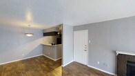 This single-floor residence in Lancaster offers a straightforward and functional layout designed for comfortable everyday living. The main living area greets you upon entry through a classic paneled white front door, opening into an open-concept space with rich, dark hardwood-style flooring that runs throughout. The neutral gray walls provide a clean, modern backdrop that complements the warm tones of the flooring.

A kitchen pass-through counter connects the cooking area to the living and dining space, creating an open and sociable flow between rooms. The kitchen features dark upper cabinetry, track lighting mounted on the ceiling, and a tiled backsplash, giving it a sleek and practical character. The pass-through design allows for easy interaction between the kitchen and the adjacent living area.

The living and dining space is well-proportioned, with smooth white ceilings that enhance the sense of openness. A hanging pendant light adds a subtle decorative touch near the dining area. White baseboards frame the floors throughout, providing a crisp contrast to the gray walls and dark flooring. Overall, this single-level home presents a clean, move-in-ready environment with a cohesive design aesthetic suited to a variety of lifestyles.