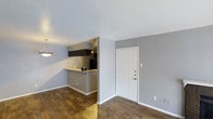 This single-floor residence in Lancaster offers a straightforward and functional layout designed for comfortable everyday living. The main living area greets you upon entry through a classic paneled white front door, opening into an open-concept space with rich, dark hardwood-style flooring that runs throughout. The neutral gray walls provide a clean, modern backdrop that complements the warm tones of the flooring.

A kitchen pass-through counter connects the cooking area to the living and dining space, creating an open and sociable flow between rooms. The kitchen features dark upper cabinetry, track lighting mounted on the ceiling, and a tiled backsplash, giving it a sleek and practical character. The pass-through design allows for easy interaction between the kitchen and the adjacent living area.

The living and dining space is well-proportioned, with smooth white ceilings that enhance the sense of openness. A hanging pendant light adds a subtle decorative touch near the dining area. White baseboards frame the floors throughout, providing a crisp contrast to the gray walls and dark flooring. Overall, this single-level home presents a clean, move-in-ready environment with a cohesive design aesthetic suited to a variety of lifestyles.
