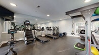 Located at 1871 Ashley River Rd in Charleston, South Carolina, this fitness center offers a well-appointed exercise space designed to support a wide range of workout routines. The single-floor layout is efficiently organized, providing ample room to move between equipment zones without feeling cramped.

The cardio section features multiple treadmills, elliptical machines, a stair climber, and a stationary bike, all positioned along a full-length mirrored wall that enhances the sense of openness and allows users to monitor their form. Recessed lighting throughout the ceiling provides bright, even illumination, while a ceiling fan contributes to airflow and comfort during workouts.

A central multi-functional training rig serves as the focal point of the space, stocked with stability balls, kettlebells, resistance bands, TRX suspension trainers, and medicine balls, catering to functional and cross-training exercises. A cable machine and dumbbell rack are also present, rounding out the strength training options.

Natural light filters in through windows and a set of glass double doors that open to an outdoor area, lending the space an airy, welcoming atmosphere. The durable rubber flooring provides both safety and comfort underfoot. Overall, this fitness center is thoughtfully equipped and designed to meet diverse training needs in a clean, modern environment.