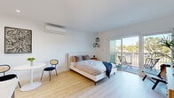 Located at 3910 Chapman St in San Diego's Ocean Beach neighborhood, this single-story studio unit offers a thoughtfully designed open-concept layout with a clean, modern aesthetic. Light wood-tone flooring runs throughout, complementing the bright white walls and creating a cohesive, airy atmosphere.

The main living area seamlessly integrates sleeping, dining, and living functions. A full bed with a stylish upholstered headboard anchors the space, accompanied by a stacked wire pendant light fixture that serves as a decorative focal point. A wall-mounted flat-screen TV and mid-century-inspired wood dresser provide functional yet attractive furnishings. A small dining area with a round white pedestal table and modern chairs completes the living space.

Floor-to-ceiling sliding glass doors open onto a private balcony with outdoor seating, offering neighborhood views and abundant natural light. A wall-mounted mini-split HVAC unit ensures year-round climate control.

The kitchen features white shaker cabinetry, a white quartz countertop, stainless steel appliances including a refrigerator, electric range, and microwave, and a peninsula that defines the space.

The bathroom is finished with a white vanity, marble-look quartz countertop, brushed gold hardware, and a mirrored medicine cabinet.
