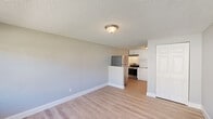 Located at 101 Mosswood Circle in Winter Springs, Florida, this single-floor unit offers a practical and efficiently designed layout comprising a living room, kitchen, bathroom, and closet. Throughout the space, light wood-tone flooring provides a clean, cohesive look, while neutral gray walls and white baseboards contribute to a bright, understated aesthetic. Textured popcorn ceilings with flush-mount light fixtures are consistent across the rooms.

The living room is a well-proportioned open area bathed in natural light from a large picture window, which also features a wall-mounted HVAC unit beneath it. The space connects openly to the kitchen, which is separated by a partial dividing wall. The kitchen is equipped with stainless steel appliances, including a refrigerator and electric range, set against white cabinetry and under-cabinet lighting. A closet with bi-fold white panel doors provides convenient storage.

The bathroom includes a tiled tub-shower combination with classic white subway tiles, a toilet, a vanity with under-sink storage, and wood-tone flooring that matches the rest of the unit. Outside, a white picket fence encloses a small private area adjacent to the unit, set against a landscaped green exterior with mature trees and open sky views.