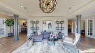 Located at 4216 S Bowman Rd in Little Rock, Arkansas, this single-floor community clubhouse offers a thoughtfully designed amenity space that blends modern style with practical functionality. The grand entrance sets an impressive tone with soaring vaulted ceilings, ornate wrought iron doors framed by an arched transom window, and rich hardwood-style flooring that carries throughout the facility. A striking spherical chandelier anchors the main lounge, where a spacious seating area is adorned with contemporary abstract artwork, open metal shelving, and refined décor. An additional lounge provides a relaxed gathering spot with warm leather accents, wood bookshelves, and a wall-mounted TV. The catering kitchen features dark granite countertops, white cabinetry, a beverage cooler, and a communal dining table beneath a modern gold-toned chandelier—ideal for events and social gatherings. The fitness center is well-equipped with a comprehensive selection of strength machines set against crown-molded walls. Adjacent to it, a dedicated spin studio houses multiple stationary bikes, built-in shelving, and an open-concept layout with a full-glass garage door that floods the space with natural light. Completing the amenity offering is a private theater room, distinguished by its dark, moody palette, snack bar, popcorn machine, and ornate entry door, creating an immersive cinematic experience.