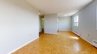 This efficiently designed one-bedroom, one-bathroom unit offers a smart and functional layout across a single floor. The space is characterized throughout by warm parquet wood flooring in a classic basketweave pattern, lending a timeless aesthetic to every room.

The open main living area is bright and airy, with soft grey walls and multiple windows that invite natural light while offering outdoor views. Baseboard heating units are present along the walls, ensuring year-round comfort. The room provides a clean, versatile canvas well-suited for a variety of furniture arrangements.

The kitchen is equipped with white cabinetry, a countertop workspace, and essential appliances including a range, making it a practical space for everyday cooking. The adjacent dining area benefits from its own window with outdoor views, continuing the light and open feel found throughout the unit.

The bedroom is generously proportioned relative to the overall footprint, featuring the same parquet flooring, grey walls, and ample natural light from a large window. The full bathroom includes a soaking tub with white tile surround, a vanity with dark cabinetry and mirror, and standard fixtures — providing a clean and functional space. Overall, the unit offers a well-organized and practical living environment.