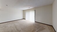 This single-floor residence offers a practical and comfortable layout designed to maximize functionality across its living spaces. The living area is generously sized, featuring neutral-toned carpet, a textured ceiling, and a full-width sliding glass door fitted with vertical blinds that floods the room with natural light and provides access to an outdoor area with greenery views.

The kitchen is well-appointed with warm, dark wood cabinetry featuring decorative scalloped trim, white appliances including a refrigerator, dishwasher, and range, a double basin sink, and light wood-look flooring that adds a clean, bright contrast to the cabinetry.

The bedrooms are carpeted and finished with neutral walls, dark wood baseboards, and vertical blind-covered windows that allow for adjustable natural light. At least one bedroom includes a sliding wood-panel closet with a hanging rod for storage. A second, more compact bedroom also features window access and ample wall space.

The primary bathroom includes a full tiled tub-shower combination with chrome fixtures, while a secondary bathroom features a toilet with a safety grab bar. A convenient stacked washer and dryer unit is tucked into a dedicated closet space within the main living area, adding valuable in-unit laundry functionality.