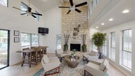 Located at 2534 Central Dr in Bedford, TX, this single-floor space makes an immediate impression with its dramatic, soaring ceilings that amplify the sense of openness throughout. The centerpiece of the main living area is a striking floor-to-ceiling natural stone fireplace, lending warmth and a bold architectural focal point to the room. Light-toned hardwood flooring runs throughout, complementing the crisp white walls and contributing to the bright, airy atmosphere. Generous windows on multiple walls flood the interior with abundant natural light while offering views of the surrounding outdoor environment. The living area is thoughtfully designed with ample seating space and is anchored by a ceiling fan that adds both function and style. Adjacent to the living area, a dedicated dining space accommodates a full-sized dining table, with a wall-mounted television positioned for easy viewing. The kitchen features rich, dark wood cabinetry, dark granite countertops, a tile backsplash, stainless steel appliances, and a raised breakfast bar that provides an open connection to the living spaces. Recessed lighting throughout ensures the interior remains well-lit. The overall ambiance is modern, welcoming, and well-suited for both everyday use and entertaining.