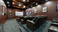 Located in Kannapolis, NC, this purpose-built screening room delivers a true cinema experience in a compact, well-appointed space. The room is designed with a classic movie theater aesthetic, featuring deep burgundy walls accented by warm wood crown molding and baseboards that add a refined, upscale feel throughout.

Seating is arranged in tiered rows of plush, dark brown leather recliners, each equipped with built-in cup holders, ensuring comfort for every viewer regardless of their seat. The raised rear platform provides unobstructed sightlines to the large front projection screen, which anchors the main wall and serves as the focal point of the room.

Overhead, a coffered ceiling with recessed can lighting provides both ambient and accent illumination, creating a cinematic atmosphere. A ceiling-mounted projector delivers crisp, large-format visuals onto the screen. A subwoofer and in-ceiling speakers support an immersive audio experience.

The walls are adorned with framed movie posters — including titles such as Kill Bill, Hamilton, and Moana — lending a fun, curated gallery feel to the space. Patterned carpet in blue-gray tones covers the floor, complementing the room's rich color palette. A popcorn cart near the screen adds a charming, authentic theater touch. The room is accessed via a solid fire-rated door with emergency exit signage, underscoring its professional-grade design.