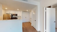 This well-appointed single-floor unit offers a clean, modern aesthetic defined by bright white walls, recessed lighting, and warm wood-tone flooring that flows throughout the main living areas. The open-concept layout seamlessly connects the kitchen and living space, creating a comfortable and functional environment. The kitchen is thoughtfully designed with two-tone cabinetry — crisp white upper cabinets paired with rich walnut-finish lower cabinets — complemented by light quartz countertops, a subway tile backsplash, and a full suite of stainless steel appliances including a gas range, microwave, refrigerator, and dishwasher. A pass-through counter with a sink connects the kitchen to the living area, enhancing the open flow of the space. The living area is generously proportioned, bathed in ambient light, and features track lighting as a stylish focal point. The bedroom offers plush carpeting, a window with natural light, and a relaxed, restful atmosphere. The full bathroom is finished with large-format tile flooring, a dark wood vanity with an illuminated mirror, quartz countertop, and a glass-enclosed soaking tub and shower combination. A louvered closet door and dedicated entry area complete this well-designed residence.