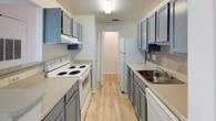 This single-floor residential unit offers a thoughtfully laid-out living space with a clean, neutral aesthetic throughout. The living area greets you at the entrance with light wood-look flooring, white walls, and a sliding glass door fitted with vertical blinds that allows natural light to fill the room. A pass-through opening connects the living area seamlessly to the kitchen, enhancing the open feel of the space.

The galley-style kitchen is well-appointed with blue-gray cabinetry on both sides, light countertops, a tile backsplash, and wood-look flooring. It is equipped with a white electric range, refrigerator, dishwasher, and a stainless steel sink, with ample upper and lower cabinet storage throughout.

The bedrooms are carpeted and bright, each featuring a window with blinds that invites natural light and a textured ceiling. The rooms offer a versatile, move-in-ready canvas for personalization.

Two full bathrooms serve the unit, each featuring a tub and shower combination. One bathroom showcases white subway tile surround, a vanity with a countertop sink, and a mirror, while the second maintains a similarly clean, functional design with neutral finishes. Both bathrooms are finished with tile-look flooring, contributing to the overall cohesive style of the home.