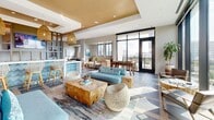 Located at 2511 Willowick Rd in Houston's upscale River Oaks area, this thoughtfully designed amenity lounge offers a sophisticated and inviting atmosphere across a single, expansive floor. The open-concept layout flows seamlessly from one zone to the next, anchored by a striking combination of slate-toned tile and warm wood-inlay flooring that runs throughout the entire space.

The living area is elegantly furnished with plush, coastal-inspired seating — including a teal sofa, natural teak coffee table, and woven rattan accent chairs — all bathed in abundant natural light streaming through dramatic floor-to-ceiling windows. These oversized glass panels frame sweeping views of the Houston skyline, bringing the city's energy directly into the space.

A stylish open bar and kitchenette area features warm wood cabinetry, white countertops, woven pendant lighting, and blue mosaic tile accents, creating a refined focal point. A custom open-shelving partition with an integrated flat-screen TV elegantly divides the lounge from the game room, which is equipped with a billiards table and shuffleboard. Tray ceilings with warm gold accents add architectural depth overhead, while recessed lighting ensures a polished ambiance throughout. Glass doors open to an adjoining outdoor terrace, further extending the sense of space and connection to the surrounding cityscape.