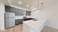 Located at 909 Eastside St SE in Olympia, Washington, this single-floor, two-bedroom, two-bathroom residence offers a well-designed layout with modern finishes throughout. The open-concept kitchen and living area serves as the heart of the space, where light wood-tone luxury vinyl plank flooring extends seamlessly underfoot. The kitchen is outfitted with dark wood-grain cabinetry, white quartz countertops, stainless steel appliances including a refrigerator and electric range, a wall-mounted range hood, and a peninsula with an integrated sink. Stylish pendant lights hang above the peninsula, adding a contemporary touch. The adjacent living area is bright and airy, featuring large windows that frame views of surrounding greenery and allow generous natural light to fill the room. The spacious primary bedroom continues the natural light theme with a wide window overlooking lush trees, while soft carpeting adds warmth underfoot. A closet with a sliding door provides practical storage. The second bedroom is similarly carpeted and well-lit. Both bathrooms are finished with wood-tone tile flooring, clean white walls, and dark vanity cabinetry, maintaining the cohesive modern aesthetic found throughout the residence.