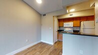 This single-story space is thoughtfully laid out, with wood-look plank flooring extending throughout the main living areas, creating a cohesive and easy-to-maintain foundation. The living room is a standout feature, benefiting from vaulted ceilings that amplify the sense of openness, along with a large sliding glass door fitted with vertical blinds that floods the room with natural light and provides outdoor views. An adjacent bedroom mirrors this brightness, featuring its own window with vertical blinds and a ceiling fan overhead.

The kitchen is positioned in an open, semi-enclosed layout visible from the main living area. It includes warm honey-toned wood cabinetry, dark countertops, and white appliances — including a refrigerator, range, microwave, and dishwasher — all arranged efficiently within the galley-style workspace. A peninsular counter separates the kitchen from the living space, offering a casual dining or prep area.

The bathroom includes a tub-shower combination with tiled surround. Neutral gray and beige tones are carried throughout the unit, contributing to a clean, understated aesthetic. The textured ceilings add a classic touch consistent across the living and bedroom spaces.