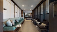 This upscale amenity lounge is thoughtfully designed to offer residents a variety of social and relaxation settings within a single, open floor plan. The space is anchored by a grand main lounge area with soaring ceilings, light wood flooring, and floor-to-ceiling windows that flood the interior with natural light and provide views of an outdoor terrace and pool beyond. A striking multi-arm globe chandelier serves as a centerpiece overhead.

The main seating area features a generously sized sectional sofa arrangement paired with sleek coffee tables, ideal for casual gatherings. Adjacent, a refined TV lounge showcases a dramatic feature wall clad in bold geometric patterned tile, framed by rich dark wood built-in shelving with integrated lighting, a wall-mounted television, and a fireplace below.

A corridor lounge offers an intimate setting with a long teal upholstered banquette along one side and individual armchairs lining the opposite wall of slatted privacy screens, lit by elegant wall-mounted sconces.

The kitchen and bar area stands out with a stunning black marble-veined island with leather bar seating, dark cabinetry, a tiled backsplash, open display shelving, and sculptural pendant lighting. A private dining nook features a herringbone accent wall, a wall-mounted screen, and booth-style seating, completing this well-appointed communal space.