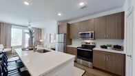 This thoughtfully designed one-bedroom, one-bathroom residence offers a cohesive open-concept layout that maximizes every square foot. The combined kitchen and living area serves as the heart of the home, featuring warm wood-toned cabinetry, white quartz countertops, a full suite of stainless steel appliances including a range, microwave, and refrigerator, and a kitchen island with bar seating — ideal for casual dining or entertaining. Light wood-style flooring runs throughout the main living areas, complementing the clean, modern aesthetic. The living room receives generous natural light through large windows with floor-to-ceiling drapes, creating a bright and welcoming atmosphere. The bedroom is a comfortable retreat, accommodating a large bed with ease, and includes a ceiling fan, a wide window with outdoor views, and access to a dedicated closet. The bathroom is well-appointed with a wood-toned vanity, a backlit mirror, white quartz countertop, and a full soaking tub and shower combination with tile surround. Additional highlights include recessed lighting throughout, two interior doors near the kitchen providing practical storage or utility access, and a hallway connecting the main living spaces to the private areas of the home.
