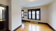 Located at 706 S Ninth St in Minneapolis, MN, this single-floor unit offers a thoughtfully designed living space with a cohesive aesthetic defined by rich dark wood trim and door frames set against crisp white walls. The main living area features warm hardwood floors that extend throughout, a large multi-pane window with bold dark framing that draws in natural light, and built-in wall shelving for added functionality. A wall-mounted mini-split unit provides climate control, while a sliding closet with dark wood panel doors offers generous storage.

The kitchen is outfitted with deep espresso-toned cabinetry, stainless steel appliances including a gas range, dishwasher, and microwave, complemented by a subway tile backsplash with decorative mosaic accents and light countertops. A hallway connects the main living space to the other areas, maintaining the consistent hardwood flooring and dark trim throughout.

The bathroom presents a refined, spa-like atmosphere with soft blue-gray walls, dark wood vanity cabinetry, a framed mirror, a walk-in glass shower with white subway tile surround, and tile flooring. The overall design of this unit balances classic architectural character with modern updates, creating a clean and inviting environment.