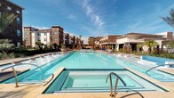 Located at 11576 Pearland Pkwy in Houston, TX 77075, this single-floor amenity facility serves a modern multi-story residential community and offers a well-rounded suite of shared spaces designed for comfort and active living.

The outdoor area is anchored by a large, resort-style swimming pool with sparkling blue water, surrounded by a spacious sun deck lined with lounge chairs. An adjacent spa provides a relaxing counterpart to the main pool. Palm trees and landscaped planters frame the area, with the residential buildings rising in the background beneath open Texas skies.

Inside, the fitness center is a standout feature, accessible via a light-filled corridor with wood-look tile flooring. The gym is enclosed by full-height glass sliding doors with black frames, offering clear sightlines into the space. Inside, a comprehensive selection of strength and cardio equipment is on hand, including weight machines, free weights, benches, and stability balls. Motivational typography murals cover the walls, reinforcing an energetic atmosphere. The facility is well-lit with overhead lighting and includes mirror walls to maximize the sense of space.

Adjacent to the fitness area, a dedicated package locker room provides secure, organized parcel storage with banks of dark metal lockers lining the walls — a practical convenience for residents. The corridor connecting these amenity spaces features clean, neutral finishes throughout, contributing to a cohesive and modern aesthetic.