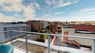This single-floor space is defined by its practical layout and a standout outdoor feature: a rooftop terrace with expansive, panoramic views of a bustling urban skyline. From the terrace, the cityscape stretches across the horizon, revealing a mix of mid-rise and high-rise buildings, mature tree canopies, and a distant church steeple beneath open skies — a compelling vantage point above the surrounding neighborhood.

The bathroom is finished in a clean, neutral palette with white walls and cream-toned cabinetry. It includes a full vanity with an integrated sink and chrome fixtures, a wall-mounted mirror with a medicine cabinet, and a shower-tub combination enclosed by a light blue patterned curtain. A chrome towel bar adds a simple, functional accent to the wall. The space is equipped with a GFCI outlet near the vanity, a ventilation vent in the ceiling, and a standard door with a knob lock for privacy.

The overall ambiance of the space is understated and utilitarian, with clean lines and minimal ornamentation throughout the interior. The rooftop terrace, accessible via the single floor, serves as the defining feature of the space, providing a strong connection to the surrounding urban environment and an open-air retreat above the city.