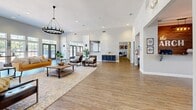 Located at 2702 N Judge Ely Blvd in Abilene, Texas, this single-floor community living room offers a generously proportioned open-plan layout designed for comfort and social gathering. The space immediately impresses with its soaring vaulted ceilings, which amplify the sense of openness and airiness throughout. Warm-toned hardwood flooring extends across the entire floor, lending a cohesive and inviting aesthetic.

Natural light is a defining feature, flooding the interior through an expansive bank of large, grid-paned windows and glass-paneled doors along one full wall, offering views of the outdoor pool area. A striking black wrought-iron chandelier anchors the main seating area, which is thoughtfully arranged with a mustard yellow sofa, leather accent chairs, and layered area rugs atop a sturdy wood coffee table ensemble.

The layout flows seamlessly into additional functional areas, including a corridor leading to supplementary rooms and a stylish blue credenza that adds a pop of color. Decorative artwork and potted greenery are placed throughout, contributing to the space's polished yet welcoming ambiance. Recessed lighting complements the natural light, ensuring the space remains bright and well-lit at all hours. Overall, this living room presents a refined, contemporary communal environment ideal for relaxation and connection.