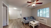 Located at 223 Rainbow Dr in the 78209 zip code of San Antonio, TX, this single-floor unit offers a practical and well-maintained layout designed for comfortable everyday living. The living area serves as the heart of the unit, featuring durable wood-look flooring, neutral gray walls, and a ceiling fan with integrated lighting that keeps the space bright and well-ventilated. A window with blinds allows natural light to filter in, contributing to a clean and airy atmosphere. The kitchen is efficiently arranged with white cabinetry, granite-style countertops, a black electric range with overhead ventilation, and a window that brings in additional natural light. The bedroom is a calm retreat, carpeted for warmth and comfort, with a ceiling fan and a large window overlooking greenery outside, providing a serene connection to the outdoors. A closet door is also visible, offering practical storage. The full bathroom is finished with wood-look flooring, a tub-shower combination with a curtain, a vanity with granite-style countertops, and neutral wall tones that create a clean, functional space. Throughout the unit, consistent finishes and a neutral color palette create a cohesive, move-in-ready environment well-suited for San Antonio living.