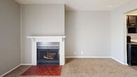 This single-floor residence offers a well-organized and functional layout designed for comfortable everyday living. The open-concept living and dining area is spacious and bright, featuring plush carpeting, a ceiling fan with light fixture, and a sliding glass door dressed with vertical blinds that fills the room with natural light. A standout feature of the living area is the classic wood-burning fireplace, framed by a white mantel and a red brick hearth, adding warmth and character to the space.

The kitchen is efficiently designed in a galley style, showcasing rich dark cabinetry, light-toned countertops, and wood-look tile flooring. Black appliances — including a refrigerator, electric range, and dishwasher — are seamlessly integrated, and the kitchen opens to the living area via a convenient pass-through counter with a sink.

The bedrooms are carpeted and well-lit, each equipped with a ceiling fan. Natural light enters through horizontal-blind-fitted windows, creating a calm and airy atmosphere. Neutral gray walls throughout maintain a clean, cohesive aesthetic.

The bathroom features a full-size soaking tub and shower combination with clean white surround panels, a toilet, and wood-look flooring, offering a practical and tidy space.
