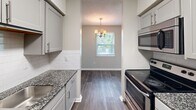 Located at 1751 Dogwood Rd in Charleston, SC, this single-floor, 2-bedroom, 2-bathroom home offers a practical and comfortable layout. The galley-style kitchen is well-appointed with gray shaker cabinets, granite countertops, a white subway tile backsplash, stainless steel appliances including an electric range and refrigerator, and durable wood-look flooring. The kitchen opens to a dining area illuminated by a classic chandelier and a window that brings in natural light. Both bedrooms feature soft wall-to-wall carpeting and ceiling fans. The primary bedroom is generously sized and includes a walk-in closet with built-in shelving, while the second bedroom offers a standard closet with a rod and natural light from a window. A connecting hallway links the two bedrooms, with each having access to its own full bathroom. Both bathrooms are equipped with tub-shower combinations featuring built-in shelving. The home's neutral color palette, textured ceilings, and consistent finishes throughout create a clean, cohesive ambiance. Two dedicated closets provide ample storage, rounding out this efficiently designed Charleston residence.