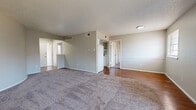 This single-floor unit offers a well-organized layout designed for comfortable living. The expansive living area is carpeted throughout and features a textured ceiling, vertical shiplap accent wall, and a set of French doors that open to a private balcony, filling the space with natural light. A secondary window provides additional brightness to the room, while the entry area transitions seamlessly from hardwood-style flooring into the carpeted living space.

The galley-style kitchen is efficiently designed with white cabinetry lining both sides, dark countertops, hardwood-style flooring, and a full suite of white appliances including a refrigerator, stove, and dishwasher. A double sink sits beneath an overhead cabinet, and a tray ceiling detail adds architectural interest above.

The bedrooms are carpeted and well-proportioned, each equipped with a ceiling fan and natural light from windows with blinds. One bedroom includes access to a walk-in closet, providing generous storage. The two bathrooms each feature a full tub-and-shower combination — one with a clean white tile surround and the other with neutral large-format beige tile — along with hardwood-style flooring. The overall aesthetic is neutral and move-in ready, with a clean, functional design throughout.