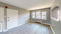 Located at 1120 N 66th St in Philadelphia, PA 19151, this 2-bedroom, 1-bathroom unit offers a clean, modern aesthetic with a thoughtfully designed single-floor layout. The open living room is bright and welcoming, featuring light wood-style luxury vinyl flooring, neutral gray walls, crisp white baseboards, and recessed lighting. A pass-through window connects the living area to the kitchen, which is equipped with stainless steel appliances, dark cabinetry, and a large window that brings in natural light. A distinctive arched entryway leads from the living room into the hallway, adding an elegant architectural detail to the space. Both bedrooms continue the consistent flooring and neutral color palette; the primary bedroom is a generous size and features natural light from a large window, while the second bedroom includes a radiator heater and an additional window with neighborhood views. The bathroom is finished with large-format tile in the tub surround, white floor tiles, a pedestal sink, and a clean, minimalist design. Radiator heating units are present throughout, complementing the classic construction of the building. The overall ambiance is fresh, light, and move-in ready.