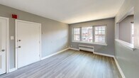 Located at 1120 N 66th St in Philadelphia, PA 19151, this 2-bedroom, 1-bathroom unit offers a clean, modern aesthetic with a thoughtfully designed single-floor layout. The open living room is bright and welcoming, featuring light wood-style luxury vinyl flooring, neutral gray walls, crisp white baseboards, and recessed lighting. A pass-through window connects the living area to the kitchen, which is equipped with stainless steel appliances, dark cabinetry, and a large window that brings in natural light. A distinctive arched entryway leads from the living room into the hallway, adding an elegant architectural detail to the space. Both bedrooms continue the consistent flooring and neutral color palette; the primary bedroom is a generous size and features natural light from a large window, while the second bedroom includes a radiator heater and an additional window with neighborhood views. The bathroom is finished with large-format tile in the tub surround, white floor tiles, a pedestal sink, and a clean, minimalist design. Radiator heating units are present throughout, complementing the classic construction of the building. The overall ambiance is fresh, light, and move-in ready.