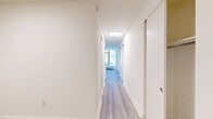 Located at 10 Hanover Place in New York City, Unit 02T is a efficiently designed 450-square-foot studio apartment spread across a single floor. The open-plan layout seamlessly integrates the kitchen and living area, maximizing every inch of the available space.

The living area features light wood-style luxury flooring, crisp white walls, and large wood-framed windows that allow generous natural light to fill the room while offering direct views of the surrounding NYC streetscape. A wall-mounted HVAC unit ensures year-round climate control.

The kitchen is thoughtfully appointed with modern white high-gloss cabinetry, a white quartz countertop peninsula with an integrated stainless steel sink, and a full suite of stainless steel appliances including a refrigerator, gas range, built-in microwave, and dishwasher. Subway tile backsplash adds a classic touch, while recessed skylight panels provide additional overhead illumination. A tall built-in pantry cabinet offers ample storage.

A hallway connects the main living space to additional rooms, lined with sliding closet doors for convenient storage. The unit's clean, neutral palette and contemporary finishes create a bright, functional living environment well-suited for urban living in downtown Manhattan.