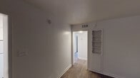 Located at 212 S Cooper St in Arlington, Texas, this single-story unit offers a clean, straightforward layout designed for practical everyday living. Wood-look flooring runs consistently throughout the space, lending a cohesive and warm aesthetic to every room.

The living area is generously sized, featuring neutral white walls, blinds for light control, and ample room for flexible furniture arrangements. A distinctive built-in shelving unit with a scalloped decorative trim and lower cabinet storage adds a charming, functional detail to the adjoining room, which also benefits from a ceiling fan with integrated lighting.

The kitchen is well-equipped with white cabinetry, dark countertops, a colorful mosaic tile backsplash, a coil-top electric range, a refrigerator, and a sink — all arranged in an efficient L-shaped layout with a window providing natural light. Overhead ventilation is also present.

The bathroom includes a full tub and shower combination with white tile surround, a toilet, and overhead storage shelving, maintaining the unit's clean, neutral color palette.

Central HVAC vents are visible throughout, ensuring climate control across all areas. The overall ambiance is simple, bright, and move-in ready, offering a functional canvas well-suited for a variety of living arrangements.