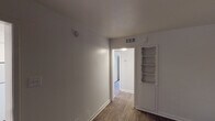 Located at 212 S Cooper St in Arlington, Texas, this single-story unit offers a clean, straightforward layout designed for practical everyday living. Wood-look flooring runs consistently throughout the space, lending a cohesive and warm aesthetic to every room.

The living area is generously sized, featuring neutral white walls, blinds for light control, and ample room for flexible furniture arrangements. A distinctive built-in shelving unit with a scalloped decorative trim and lower cabinet storage adds a charming, functional detail to the adjoining room, which also benefits from a ceiling fan with integrated lighting.

The kitchen is well-equipped with white cabinetry, dark countertops, a colorful mosaic tile backsplash, a coil-top electric range, a refrigerator, and a sink — all arranged in an efficient L-shaped layout with a window providing natural light. Overhead ventilation is also present.

The bathroom includes a full tub and shower combination with white tile surround, a toilet, and overhead storage shelving, maintaining the unit's clean, neutral color palette.

Central HVAC vents are visible throughout, ensuring climate control across all areas. The overall ambiance is simple, bright, and move-in ready, offering a functional canvas well-suited for a variety of living arrangements.