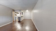 This well-organized one-bedroom, one-bathroom unit offers a practical and comfortable layout spread across a single floor. Rich, dark hardwood flooring runs throughout the main living areas and bedroom, adding warmth and a cohesive visual flow to the space.

The living room is open and airy, featuring neutral walls, a textured ceiling, and a window that invites natural light. It connects seamlessly to the kitchen via a pass-through counter with a breakfast bar overhang, making the space feel connected and social. A secondary view from the living room reveals a private entry door with an adjacent window, providing additional natural light.

The galley-style kitchen is efficiently designed with gray cabinetry, granite-style countertops, tile backsplash, and tile flooring. It is equipped with a full-size white refrigerator, an electric range with oven, and a double-basin sink — offering all essential cooking amenities in a compact, functional footprint.

The bedroom is a comfortable size, featuring a ceiling fan with a light fixture, a window with blinds, and direct access to a dedicated walk-in closet. The closet is outfitted with built-in shelving and hanging rods, providing ample organized storage.

A hallway connects the main living areas to the bedroom and bathroom, completing this thoughtfully laid-out single-floor residence.